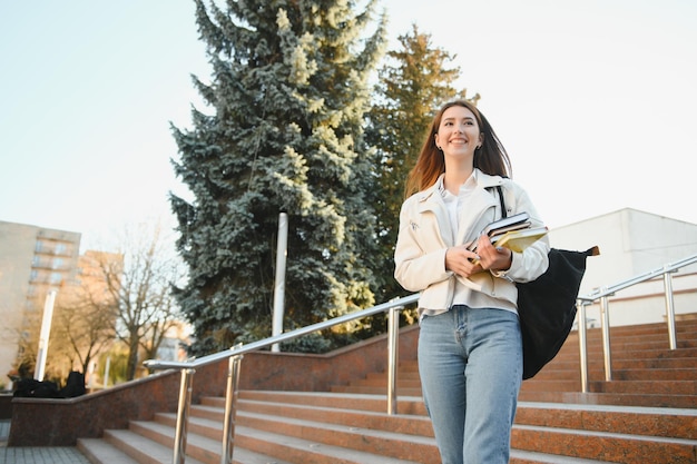 Studentessa giovane sorridente contro l'università Studentessa carina tiene in mano cartelle e quaderni Concetto di educazione all'apprendimento