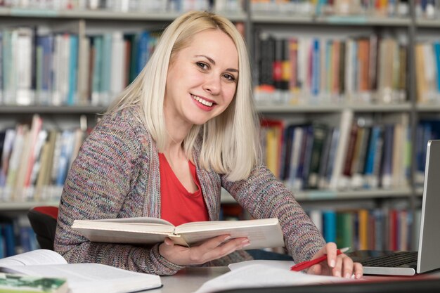 Studentessa graziosa con libri che lavorano in una biblioteca del liceo