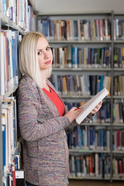 Studentessa graziosa con libri che lavorano in una biblioteca del liceo