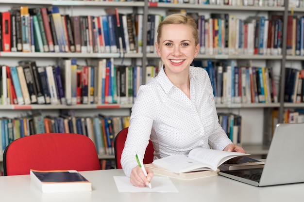 Studentessa graziosa con libri che lavorano in una biblioteca del liceo