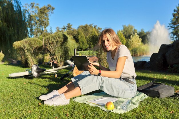 Studentessa guardando lo schermo della tavoletta digitale parlando seduto sull'erba