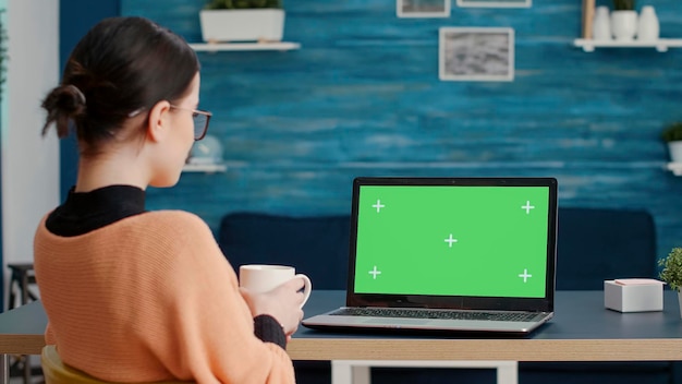 Studentessa guardando lo sfondo dello schermo verde sul laptop, lavorando con un modello di chiave cromatica vuota e uno spazio di copia mockup isolato per la lezione scolastica online. Educazione a distanza. Scatto da treppiede.