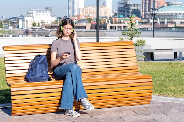 Studentessa guardando una lezione video online da un telefono cellulare su una panchina Una ragazza adolescente ascolta musica