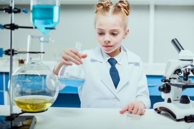 Studentessa in camice bianco che fa esperimenti con i reagenti nel concetto di studente di scienze chimiche di laboratorio