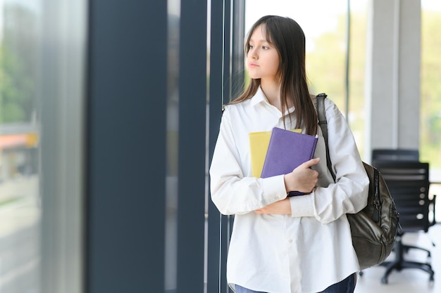 Studentessa in piedi con libri e zaino a scuola