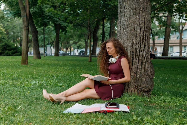 Studentessa in possesso di libro e seduta sotto l'albero