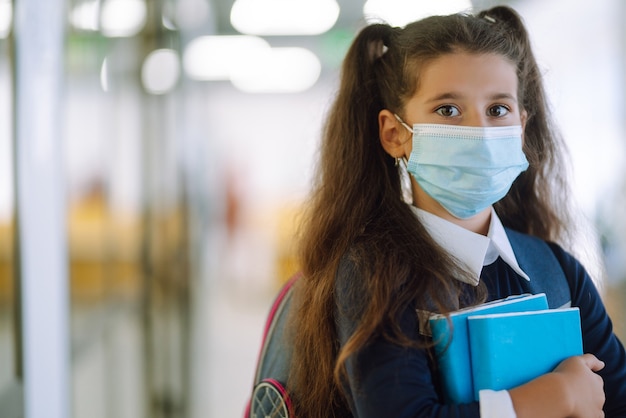 Studentessa in una maschera protettiva con uno zaino e un libro di testo.