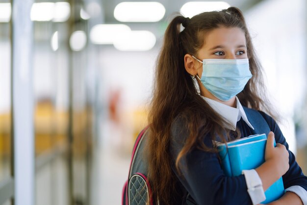 Studentessa in una maschera protettiva con uno zaino e un libro di testo.