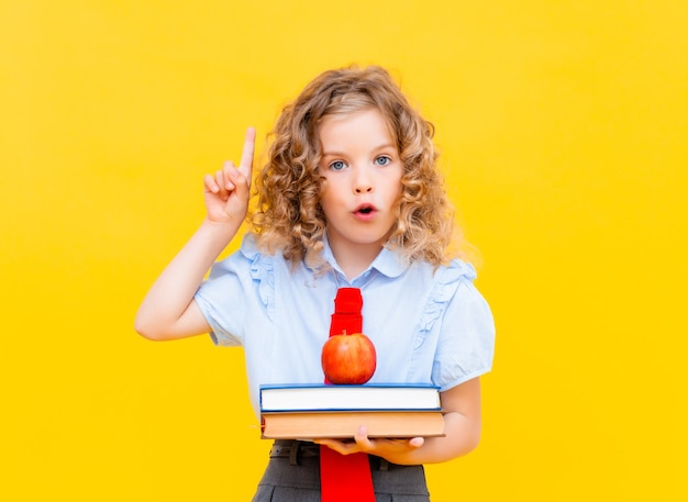 Studentessa in uniforme scolastica con in mano una pila di libri e una mela rossa su sfondo giallo. Concetto di apprendimento e scuola.