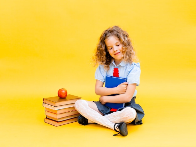Studentessa in uniforme scolastica con in mano una pila di libri e una mela rossa su sfondo giallo. Concetto di apprendimento e scuola.
