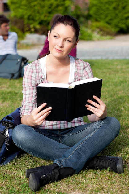 Studentessa luminosa che legge un libro che si siede sull&#39;erba