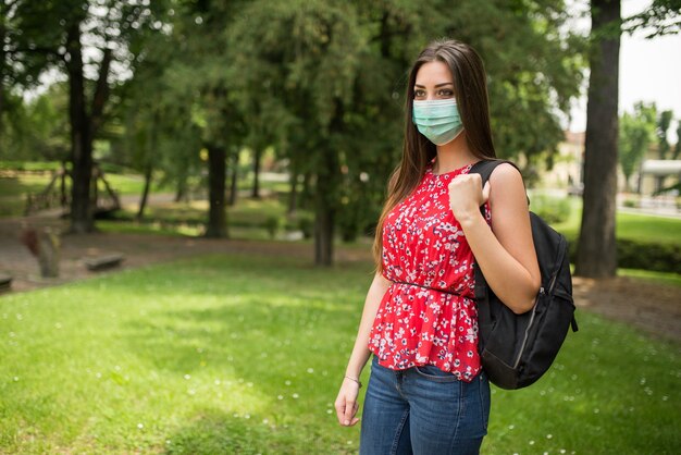 Studentessa mascherata che cammina in un parco, concetto educativo di coronavirus covid-19