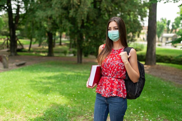 Studentessa mascherata che tiene un libro all'aperto