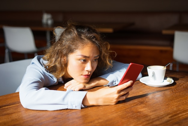 Studentessa messa a fuoco che per mezzo dello smartphone al caffè