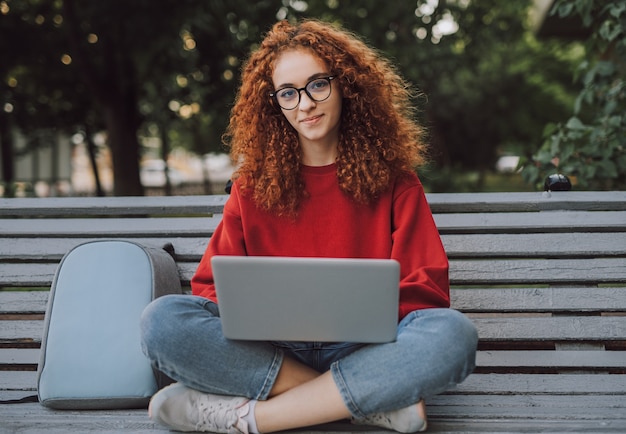 Studentessa millenaria utilizzando laptop mentre è seduto sulla panchina