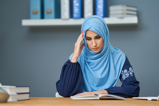 Studentessa musulmana infelice che impara in biblioteca