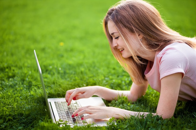 Studentessa sdraiata sull'erba con il computer portatile
