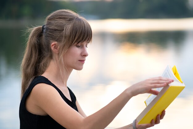 Studentessa seduta nel parco estivo che legge il libro di testo all'aperto. Istruzione e concetto di studio.