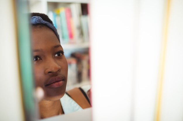 Studentessa selezionando libro da scaffale in libreria