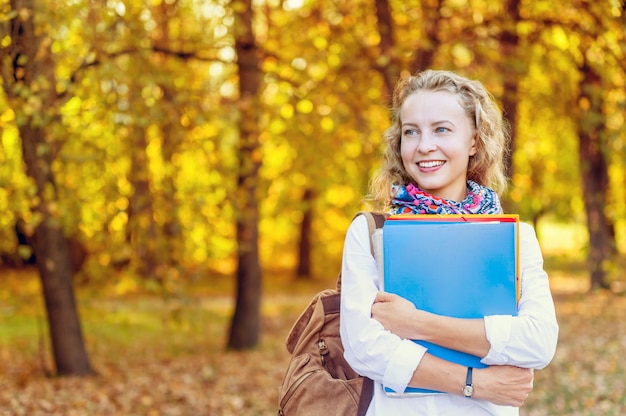 Studentessa sorridente con le cartelle nel parco di autunno