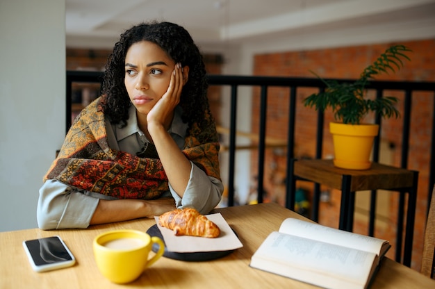 Studentessa stanca al tavolo nella caffetteria. Donna che impara una materia in caffè, istruzione e cibo. Ragazza che studia nella caffetteria del campus