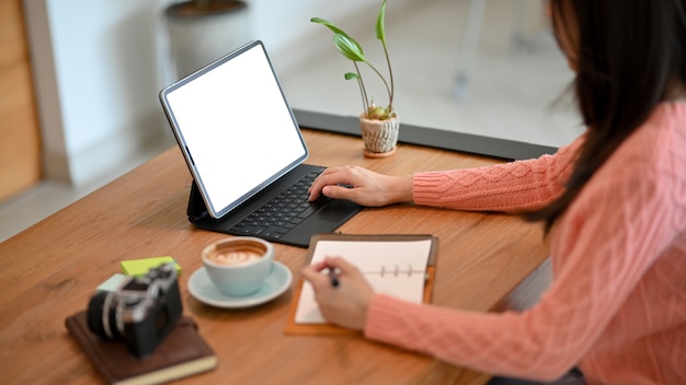 Studentessa universitaria che fa i compiti guardando sul tablet e prendendo appunti