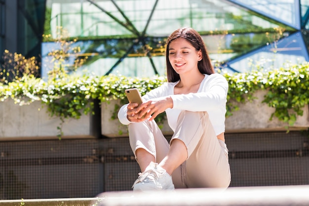 Studentessa universitaria femminile di etnia allegra che manda un sms sul suo telefono cellulare davanti a un campus