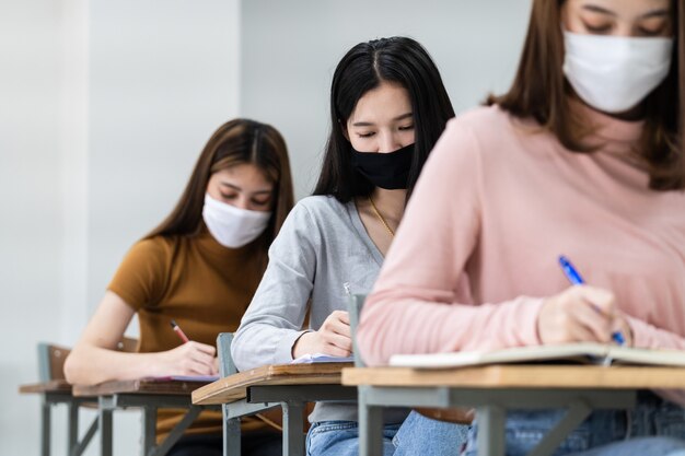 Studentesse universitarie adolescenti indossano la maschera facciale e mantengono le distanze mentre studiano in classe e nel campus universitario per prevenire la pandemia di COVID-19