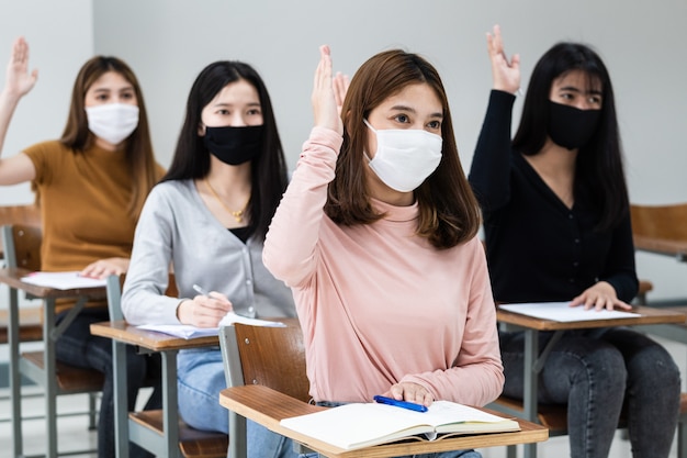 Studentesse universitarie adolescenti indossano la maschera facciale e mantengono le distanze mentre studiano in classe e nel campus universitario per prevenire la pandemia di COVID-19