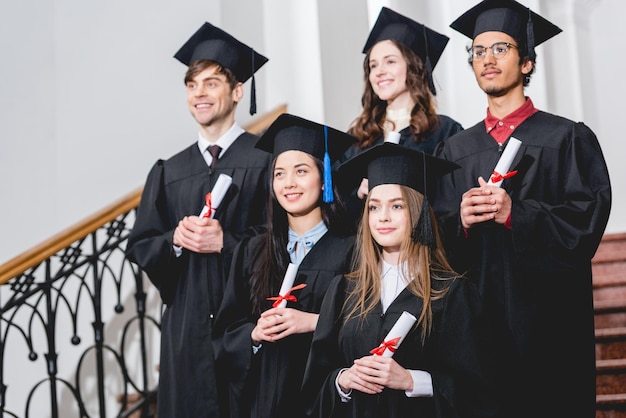 studenti allegri in abiti da laurea con diplomi all'università