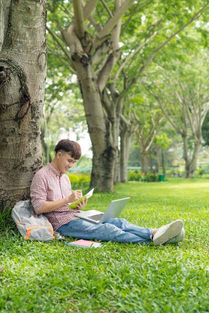 Studenti asiatici che scrivono composizioni in quaderni seduti sul prato del parco