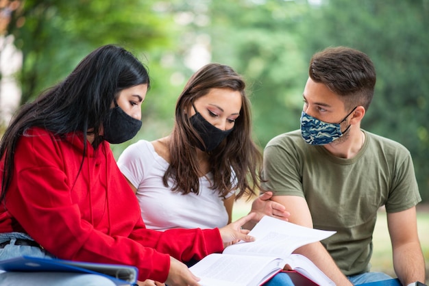 Studenti che studiano insieme seduti su una panchina all'aperto e indossano maschere durante i tempi del coronavirus