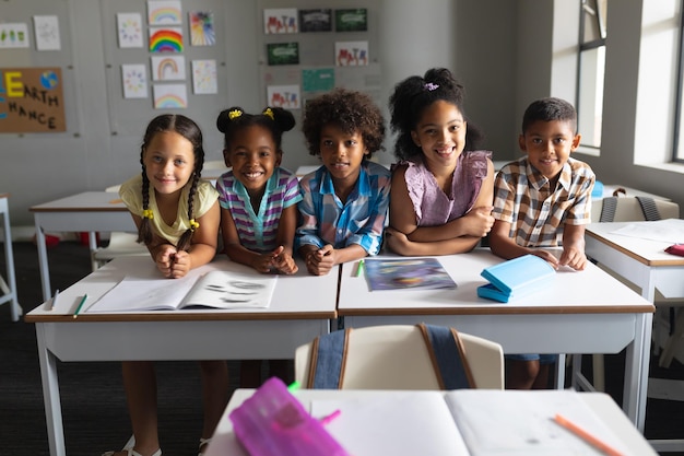 Studenti delle scuole elementari multirazziali sorridenti seduti alla scrivania in classe