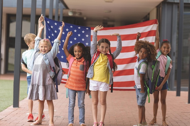 Studenti delle scuole felici in piedi nel corridoio mentre si tiene la bandiera americana