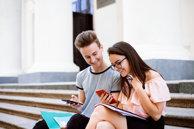 Studenti felici seduti sulle scale del college utilizzando i telefoni cellulari, mandare SMS, scattare foto