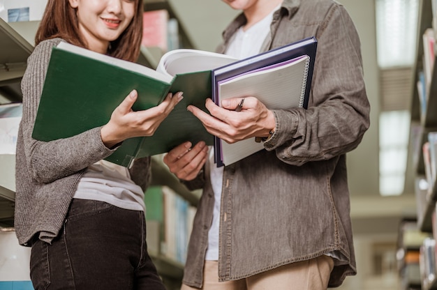 Studenti maschi e femmine che leggono libri per gli esami nella biblioteca universitaria. Concetti di istruzione, scuola, biblioteca e conoscenza.