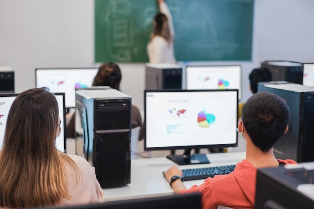 Studenti multirazziali che utilizzano computer durante la business class che indossano maschere di sicurezza a scuola Focus sulla testa del ragazzo destro