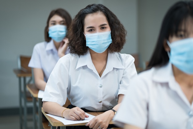 Studenti universitari allegri in classe indossano maschere protettive e usano antisettici per la prevenzione del coronavirus durante la pandemia di coronavirus. Gruppo di studenti che indossano maschere di protezione in classe.