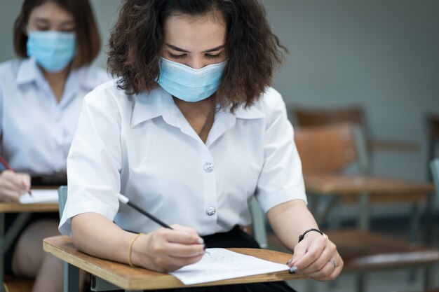 Studenti universitari allegri in classe indossano maschere protettive e usano antisettici per la prevenzione del coronavirus durante la pandemia di coronavirus. Gruppo di studenti che indossano maschere di protezione in classe.