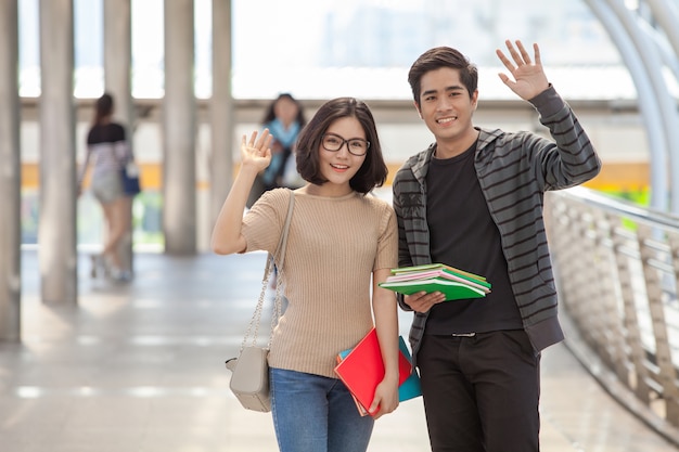 Studenti uomo e donna che tengono molti libri agitando le mani salutano i loro amici