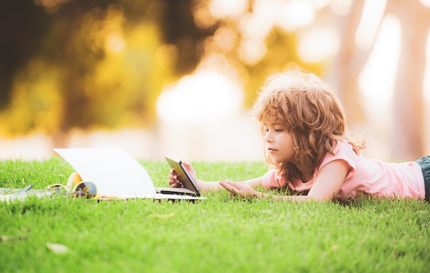 Studi sui bambini e impara con il tablet fuori dallo scolaro divertente del bambino della scuola si trova sulla distanza dell'erba lear