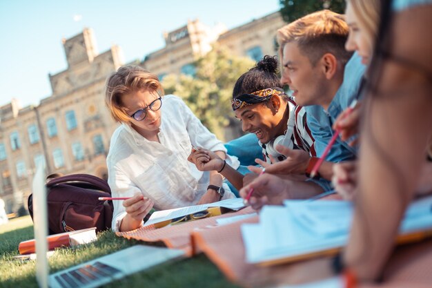 Studiare è difficile. Ragazzo concentrato sdraiato sul prato vicino ai suoi compagni di gruppo che fanno compiti difficili.