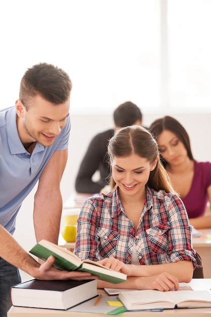 Studiare in un'atmosfera amichevole. Due studenti allegri che discutono di qualcosa mentre guardano il libro insieme ad altri studenti seduti dietro di loro