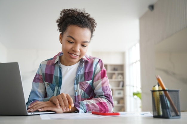 Studio di una studentessa adolescente di razza mista seduto alla scrivania con un laptop che fa i compiti Istruzione a distanza