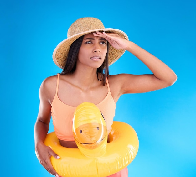 Studio donna scioccata sulla spiaggia e in vacanza su sfondo blu guardando o cerca con cappello e mano sul viso Viaggio in piscina vacanza e ragazza preoccupata con anatra di gomma gonfiabile usura dell'oceano in vacanza