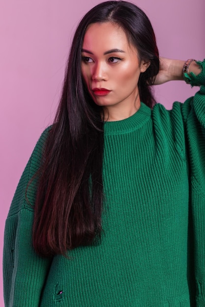 Studio glamour ritratto di una bella ragazza modello Ragazza asiatica con i capelli lunghi in un maglione alla moda verde lavorato a maglia su sfondo rosa