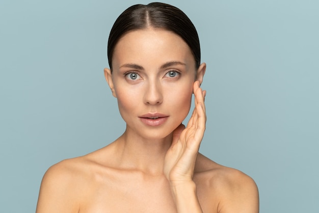 Studio Ritratto di giovane donna con trucco naturale, capelli pettinati, toccando la pelle pura ben curata