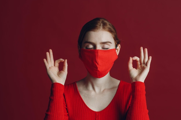 Studio ritratto di giovane donna in maschera medica protettiva isolata su sfondo rosso Yoga calma zen e meditazione un concetto di pandemia covid19