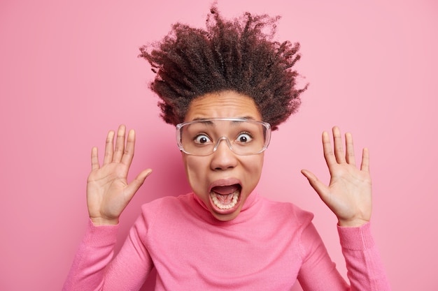 Studio scatto di una donna pazza emotiva stupefatta alza i palmi delle mani tiene la mascella abbassata fissa gli sguardi terrorizzati urla ad alta voce vestita casualmente ha i capelli sollevati