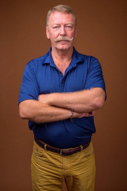 Studio shot di bell'uomo anziano con i baffi che indossa la polo blu contro il marrone